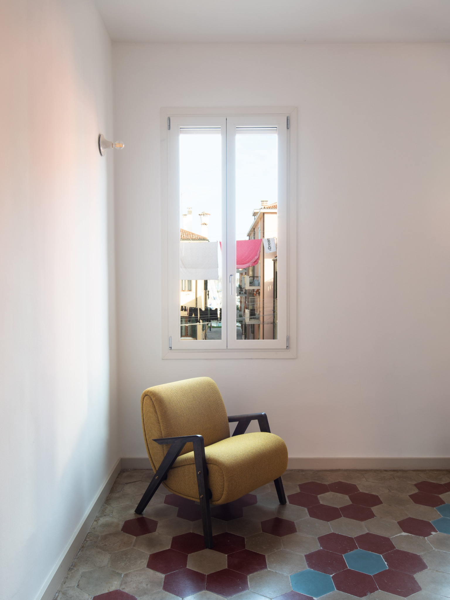Poltrona gialla su pavimento esagonale in cotto e cemento, finestra con vista